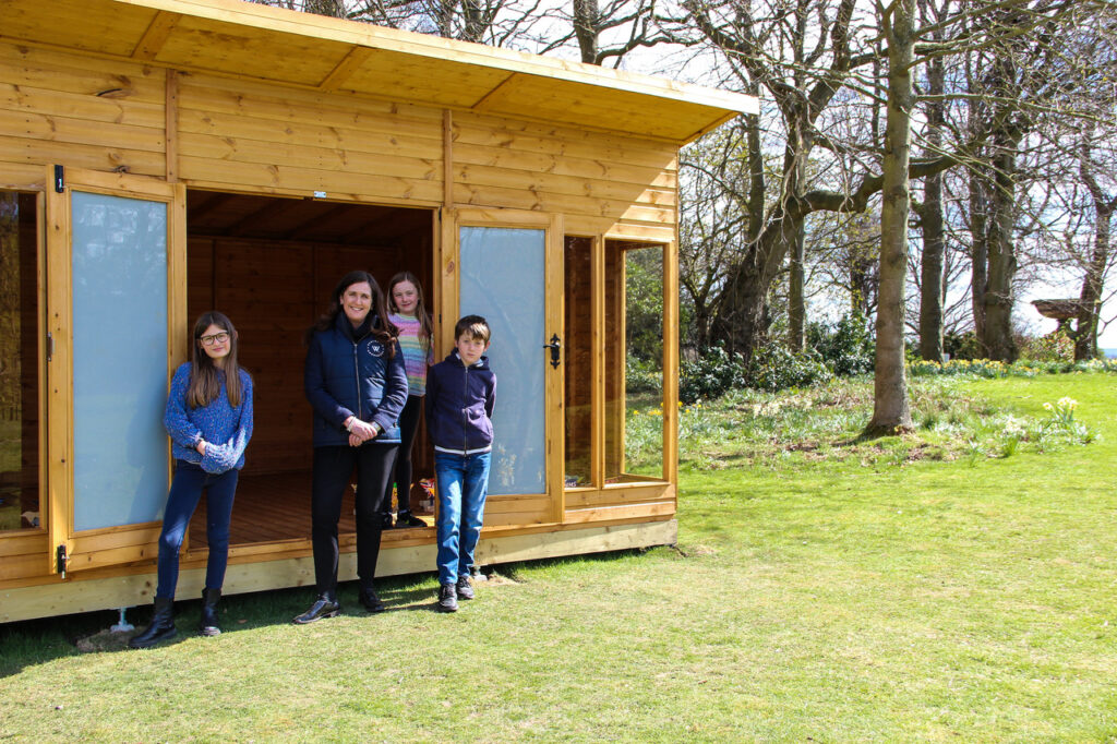 COO Paula and children in front of a wooden cabin.