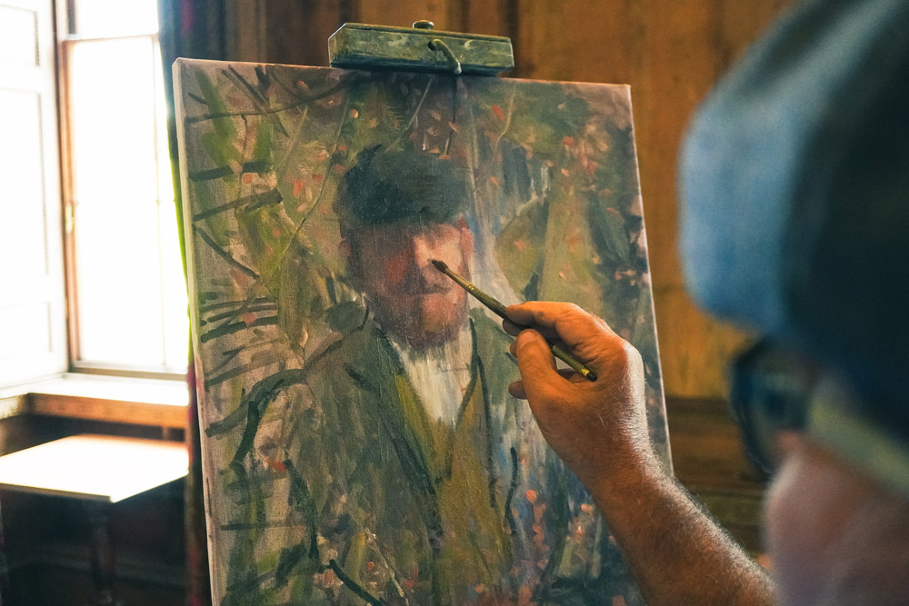 A hand holds a brush and adds the finishing touches to a portrait.